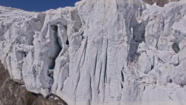 A powerful drone shot revealing massive overhanging seracs and towering ice cliffs in Saas-Fee, Switzerland. The frozen formations glisten under alpine light, showcasing the raw power of the glacier.