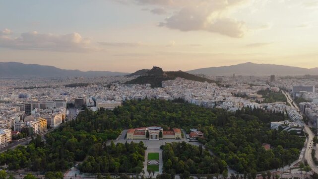 Panoramic drone shot of Zappeion Hall in Athens at sunrise with Lycabettus Hill in the background and clouds glowing in the morning sky