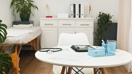 Bright Modern Medical Consultation Room With Table, Stethoscope, Tablet And Office Accessories