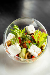 A vibrant Greek salad with fresh vegetables and cubed feta cheese, served in a modern clear glass...