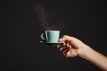 Hand holding steaming espresso cup on dark background. Barista serving hot coffee, premium cafe...