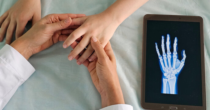 Doctor shows x-ray of hand on tablet computer to girl and child in clinic