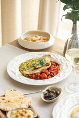 Appetizing grilled fish fillet served with green peas, tomato ragout and wine on elegant table...