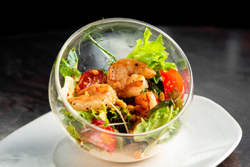 A gourmet shrimp salad served in a clear glass bowl on a white plate. The salad features grilled...