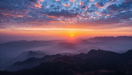 Obraz premium Aerial perspective of misty valleys and obscured summits during twilight, highlighting the sun's brilliant glow on dark mountain ridges