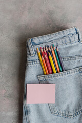 Colored pencils and an empty pink note in the back pocket of blue jeans. An idea of a female...