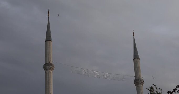 Low angle dusk view of a mosque dome and twin minarets with mahya lights reading 'Her şey fani, Allah b&acirc;k&icirc;' ('All is mortal, God remains'). Warm lamps and blue hour sky evoke reflection and faith.