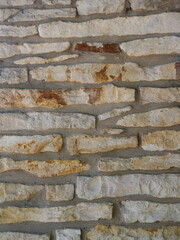 Natural stone wall with irregularly shaped stones in beige, gray, and brown shades. Gray mortar...