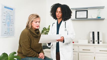 Doctor Discussing Patient Medical Report With Older Woman In Clinic Office Setting During...