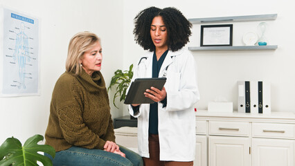 Fototapeta premium Compassionate Doctor Counsels Patient In Clinic While Using Tablet For Medical Advice