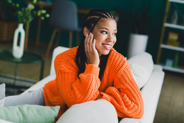 Young woman in bright orange knit sweater relaxing on a sofa at home in a cozy living room