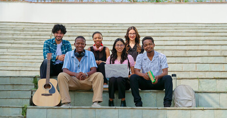 Indian young adult gen z guys male man lady female group team sitting on stair look camera spend...