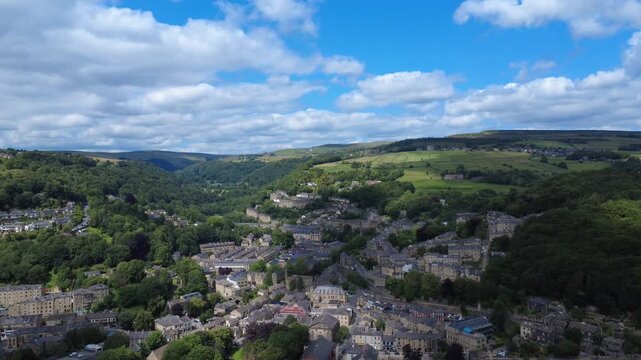 panoramic aerial view of the town of hebden bridge moving along the valley in summer sunshine surrounded by fields and hills