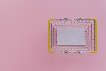 Shopping cart with a blank sheet of white paper inside on a pink background