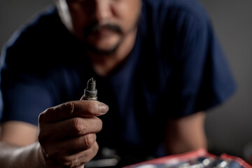 Fototapeta premium Close-up of a man’s hand holding a car spark plug, representing automotive maintenance, mechanic work, vehicle repair, and engineering technology.