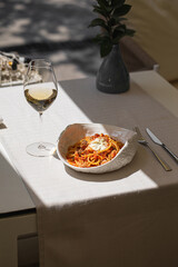 Spaghetti pasta with tomato sauce and cheese served with white wine on sunny elegant table with fork and knife