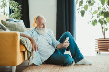 Senior man relaxing at home with headphones and phone in a cozy living room enjoying rest and smile