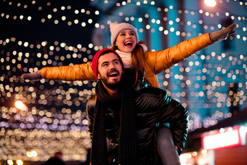 Playful couple on city street night enjoys christmas merriment with twinkling lights woman rides on...