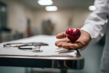 Medical professional displays a red heart model in hand, with a stethoscope resting on a table in a clinical environment