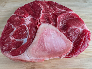 Raw beef shank cross-section with bone on wooden cutting board, detailed close-up of fresh red meat...