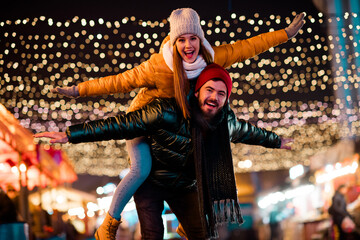Fototapeta premium Delighted couple and friend enjoy festive street lights at a winter market full of joy and holiday glow