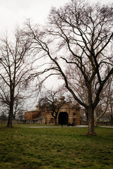 Naklejka premium Historic stone gate surrounded by tall bare trees in a park on a cloudy winter day