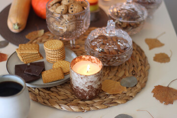 Lit candles, cookies, chocolate, nuts, tea, wine, pumpkins, books, reading glasses and autumn leaves on the table. Autumnal hygge at home. Selective focus.