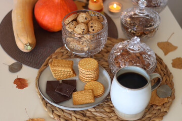 Lit candles, cookies, chocolate, nuts, tea, wine, pumpkins, books, reading glasses and autumn leaves on the table. Autumnal hygge at home. Selective focus.