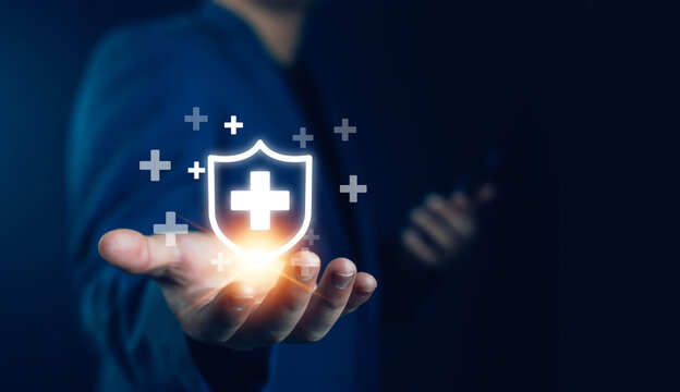 Businessman holding digital shield with medical cross icon, symbolizing health insurance protection, healthcare technology, safety, and innovation in modern digital healthcare.