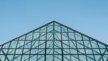 Triangular patterned glass architecture under a clear blue sky. Steel and glass facade featuring a transparent support framework.
