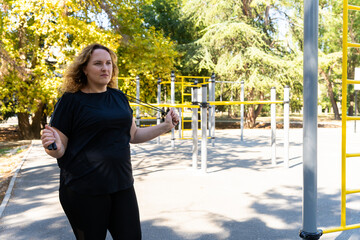 A plus-size woman wearing a black leggins and a black T-shirt is jumping rope or drinking water...