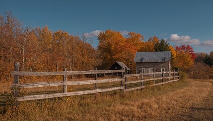 Fototapeta premium An old farmhouse surrounded by a rustic fence and autumnal trees, seasonal change
