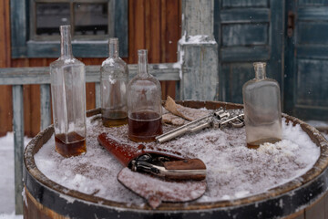 Abandoned Bottles and Revolvers on Snowy Barrel