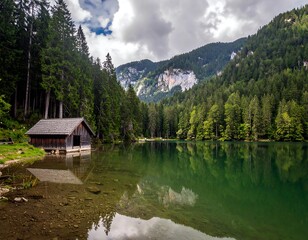 Fototapeta premium Serene lake scene with boathouse, forests, and mountains reflecting