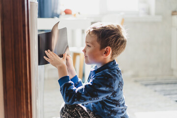 A young boy is focused on drawing on the refrigerator with a marker in a bright and inviting kitchen