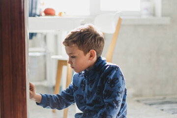 A young boy is focused on drawing on the refrigerator with a marker in a bright and inviting kitchen