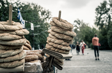 Stack of traditional sesame bagels (koulouri) displayed by a street vendor in an outdoor market with people walking in the background, capturing daily life and local food culture in the city.