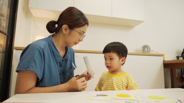 Asian mother and young son playing a fun flashcard guessing game during homeschool at home, smiling and learning new words together