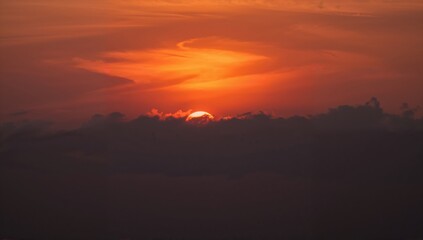 Fototapeta premium Sunset in shades of orange with a hazy sun veiled by clouds