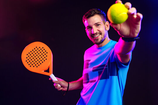 Young man plays padel tennis with racket and ball in colorful lighting