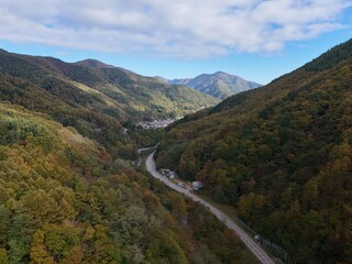 A mountain range with a road running through it. The road is surrounded by trees and the sky is blue