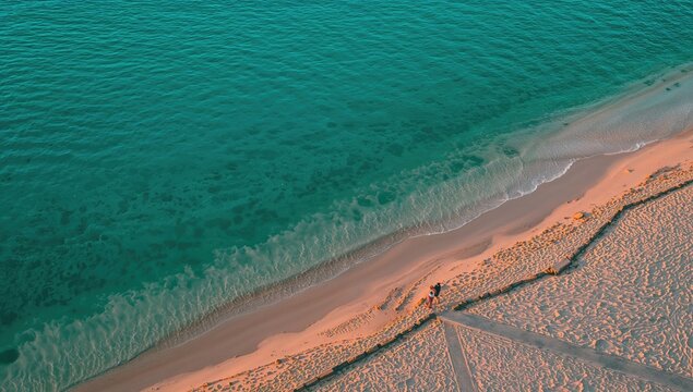 Aerial view of a couple strolling along a beach at sunset near a turquoise sea, romantic getaway, summer relaxation