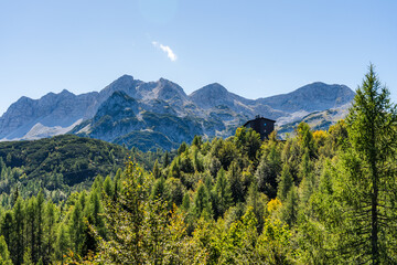 Fototapeta premium Wooded Hill with Trekking Hut in Foreground, Julian Alps in Background on a Sunny Late Summer Day