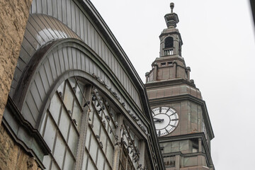 Clock tower close-up with pigeons. Detailed view of a train station clock tower with pigeons on the facade. Weathered metal and architectural detail highlight city heritage.