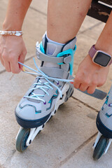 Closeup view of unrecognizable woman tying roller skates laces outdoors, wearing smartwatch on...