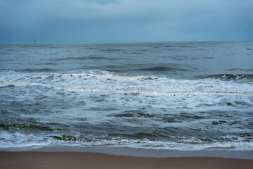 Ocean waves close-up. Foamy waves roll toward the sandy shore under a cloudy sky. The sea shows subtle blue and green tones.