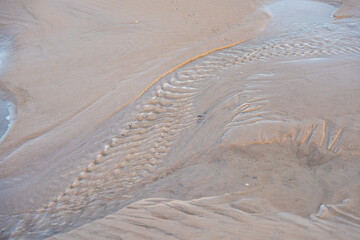 Water patterns in sand. Close-up of fine water channels and textures on wet sand. Gentle sunlight highlights natural beach formations.