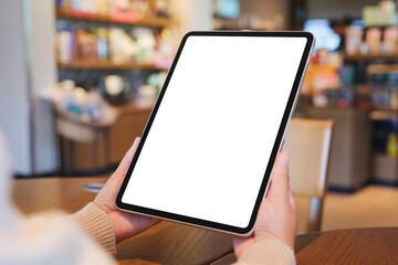 Mockup image of a woman holding digital tablet with blank white desktop screen in cafe