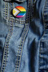 Close-up of an LGBTQ+ pride button pinned to a blue denim jacket. The badge features the inclusive Pride flag colors, symbolizing support, equality, and identity expression within the LGBTQ+ community