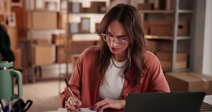 Woman, writing and laptop for ecommerce logistics, delivery and shipping info in fashion business. Person, taking notes with computer in retail office for sale, packaging details and courier service.